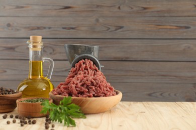 Photo of Mincing beef with manual meat grinder. Parsley, oil and spices on wooden table, space for text