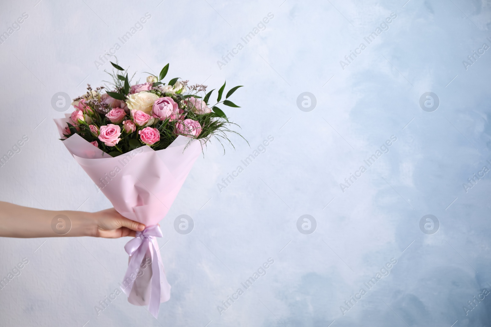 Photo of Woman with bouquet of beautiful roses on light blue background, closeup. Space for text