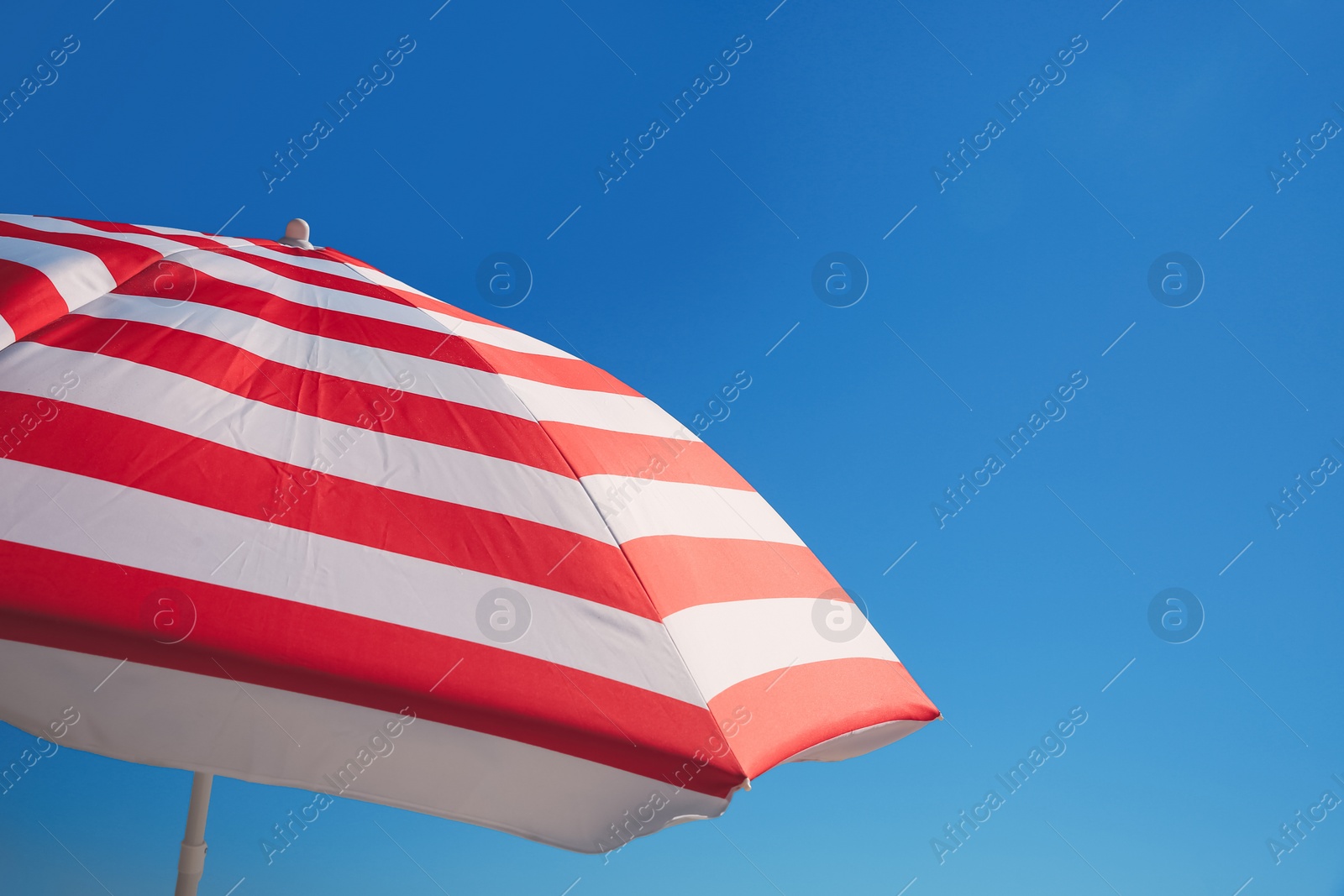 Photo of Red and white striped beach umbrella against blue sky, space for text