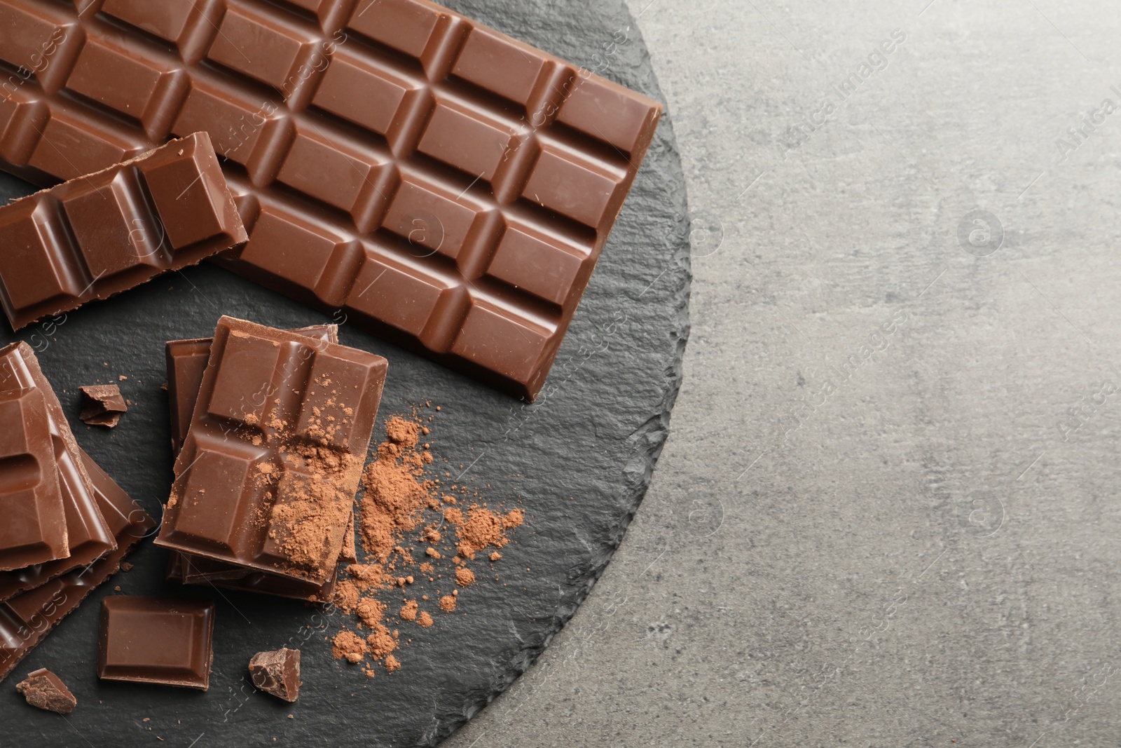 Photo of Slate plate with pieces of tasty chocolate on grey background, top view. Space for text