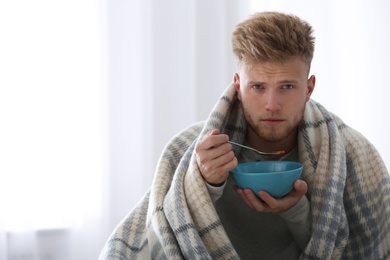 Sick young man eating soup to cure flu at home. Space for text