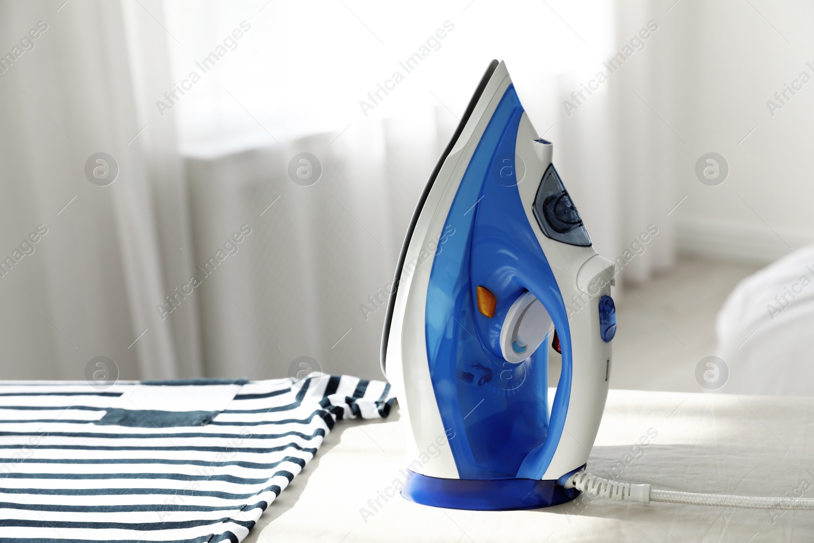 Photo of Modern electric iron on board indoors, space for text. Household appliance