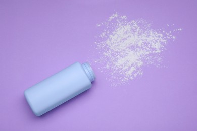 Photo of Bottle and scattered dusting powder on violet background, top view. Baby cosmetic product