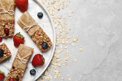 Photo of Tasty granola bars and ingredients on light grey table, top view. Space for text