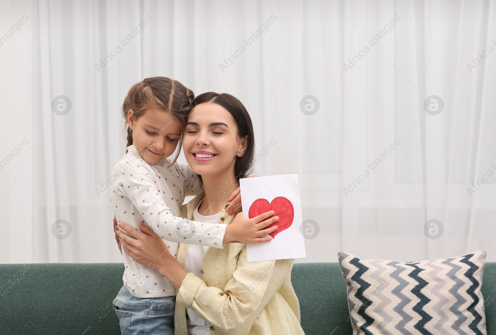 Photo of Happy woman with her daughter and handmade greeting card on sofa at home, space for text. Mother's day celebration