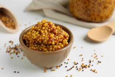 Fresh whole grain mustard in bowl and dry seeds on white table, closeup. Space for text