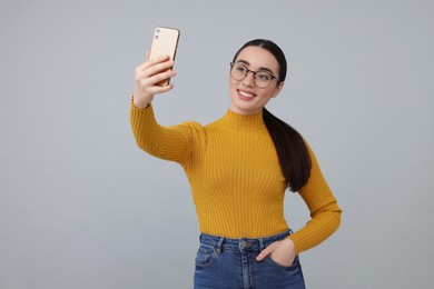 Photo of Smiling young woman taking selfie with smartphone on grey background, space for text