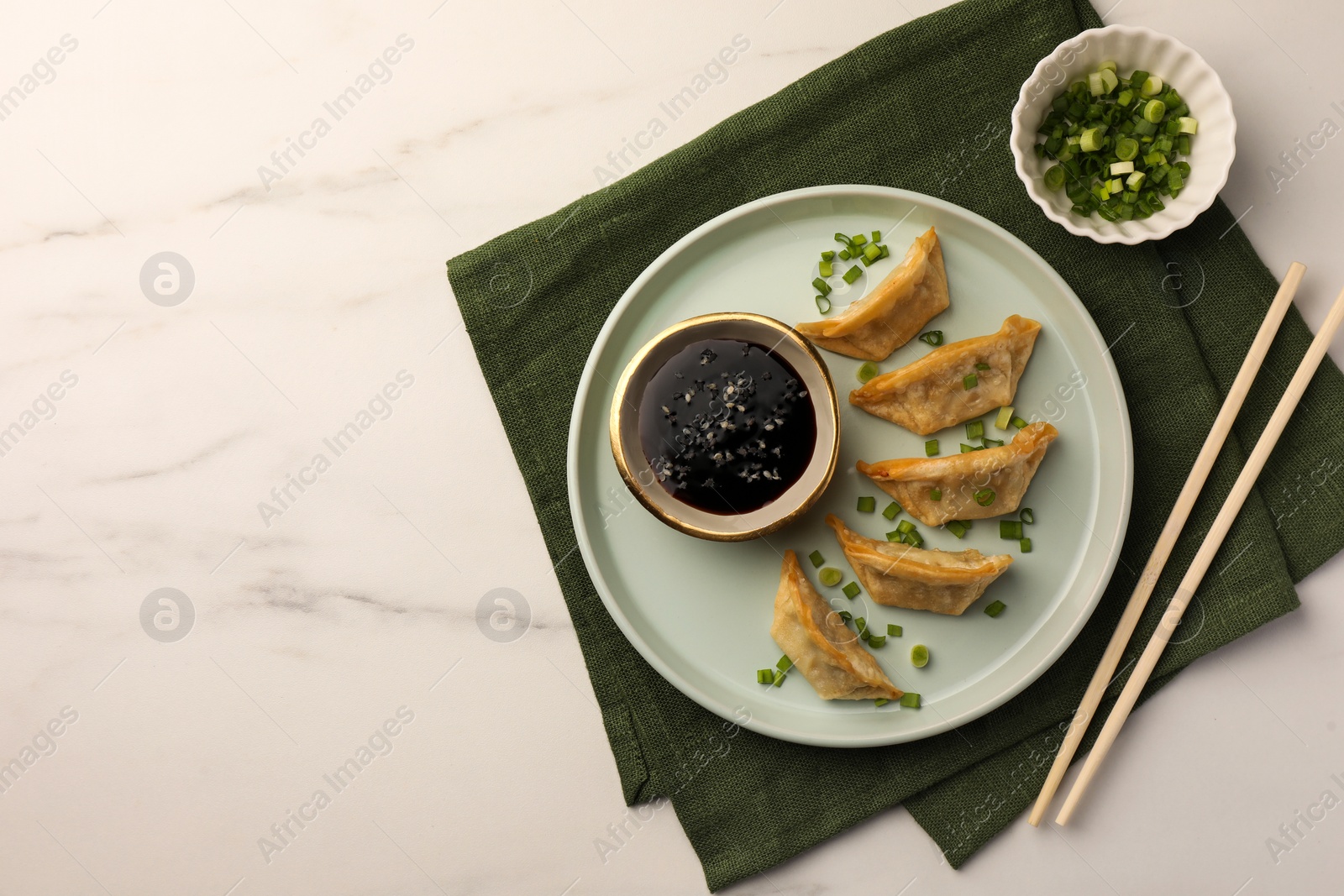 Photo of Delicious gyoza (asian dumplings) with soy sauce, green onions and chopsticks on white marble table, top view. Space for text