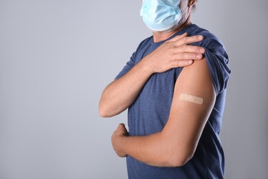 Photo of Senior man in protective mask showing arm with bandage after vaccination on grey background, closeup. Space for text