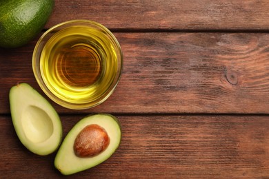 Cooking oil in bowl and fresh avocados on wooden table, flat lay. Space for text