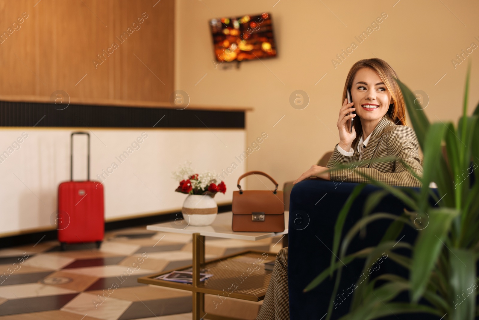 Photo of Beautiful woman talking on phone while waiting in hotel hall