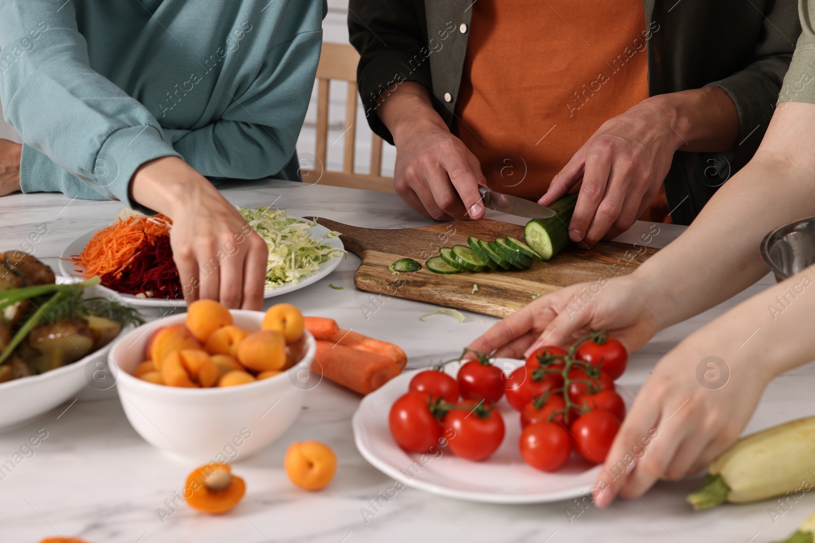 Photo of Friends cooking healthy vegetarian meal at white marble table in kitchen, closeup