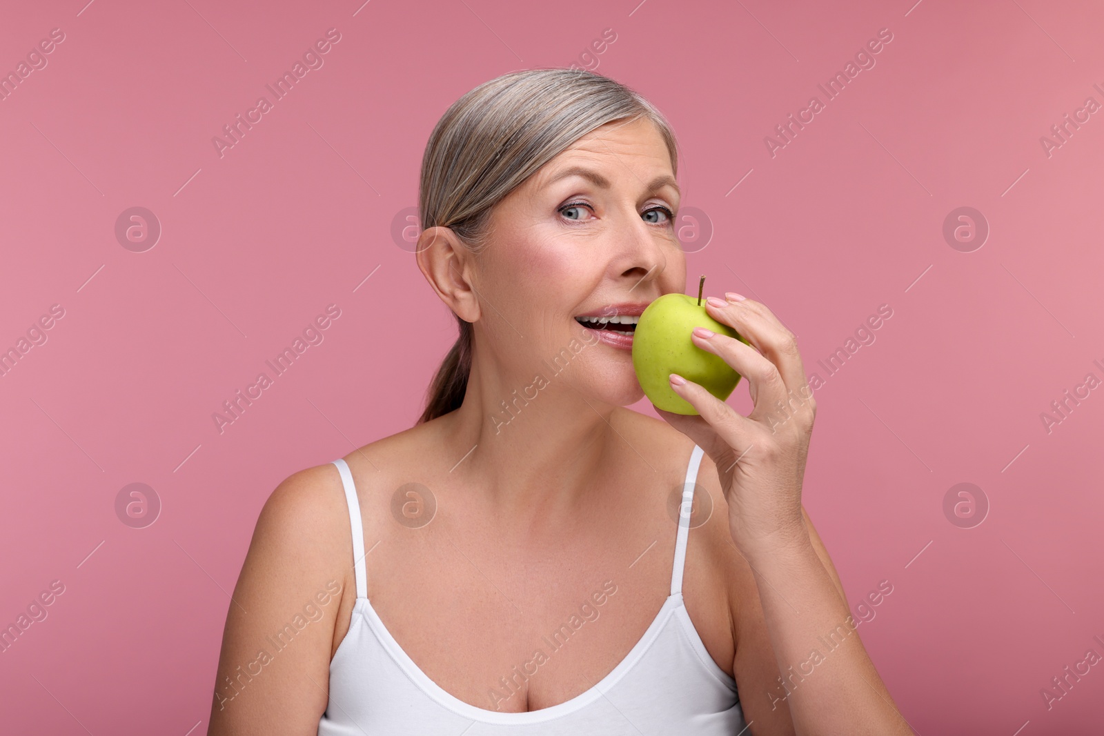 Photo of Beautiful woman eating fresh apple on pink background. Vitamin rich food