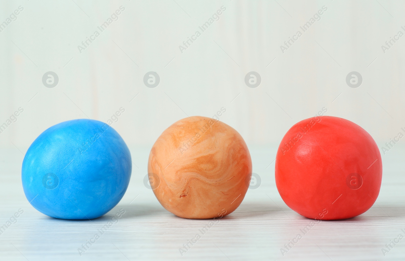 Photo of Different color play dough balls on white wooden table, closeup