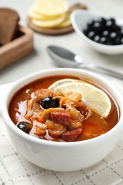 Photo of Meat solyanka soup with sausages, olives and vegetables in bowl on white table, closeup