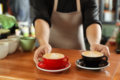 Photo of Barista putting cups of coffee on wooden table, closeup. Space for text