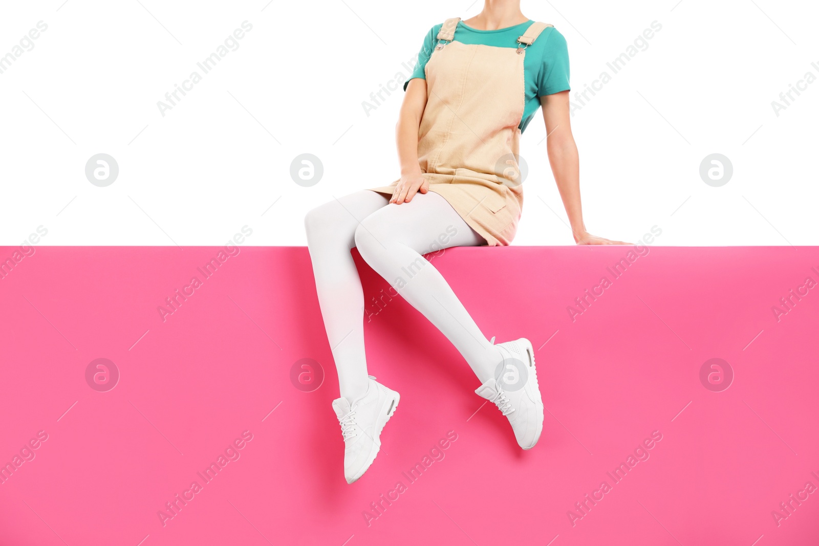 Photo of Woman wearing white tights and stylish shoes sitting on color background, closeup