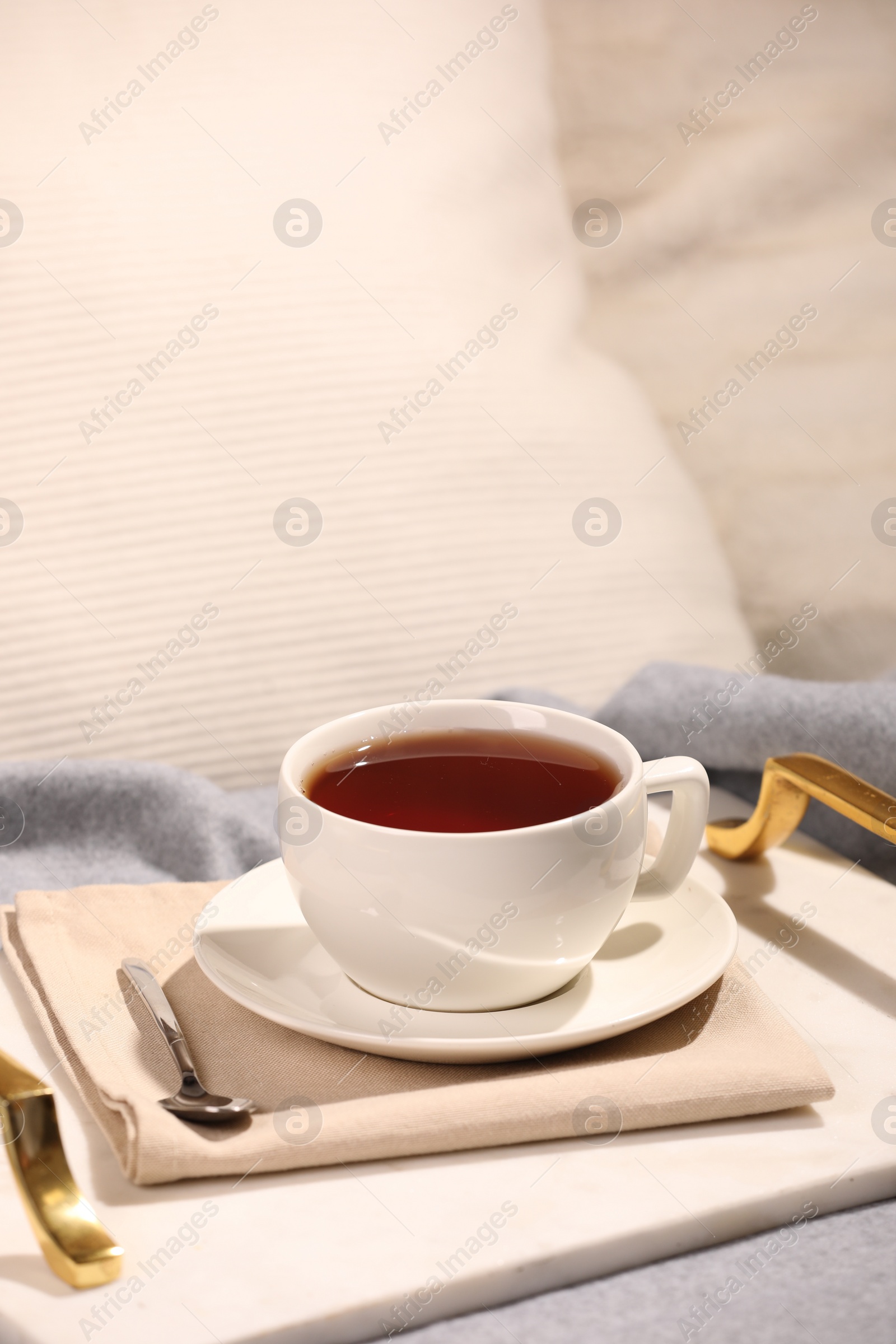 Photo of Aromatic tea in cup, saucer and spoon on bed