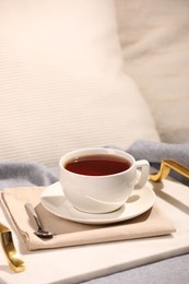 Aromatic tea in cup, saucer and spoon on bed