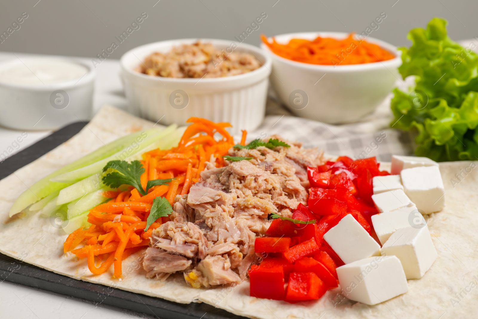 Photo of Delicious tortilla with tuna and vegetables on white table, closeup. Cooking shawarma