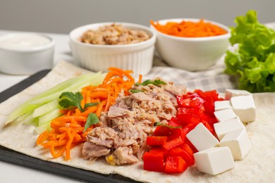 Photo of Delicious tortilla with tuna and vegetables on white table, closeup. Cooking shawarma