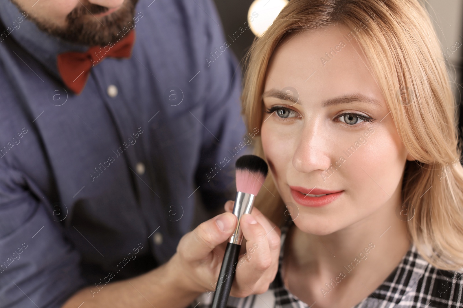 Photo of Professional makeup artist working with client in dressing room