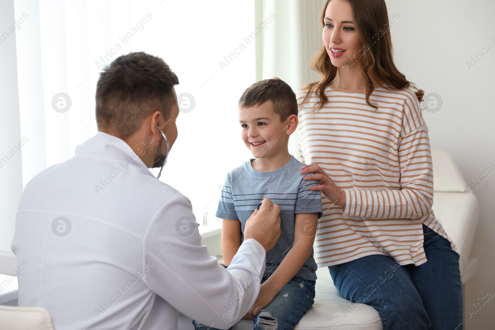 Photo of Mother and son visiting pediatrician. Doctor examining little patient with stethoscope in hospital