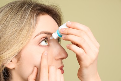Photo of Young woman using eye drops on pale olive background, closeup