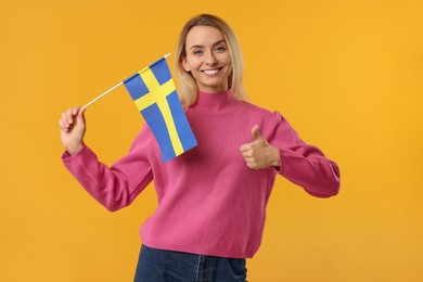 Photo of Happy woman with flag of Sweden showing thumbs up on orange background