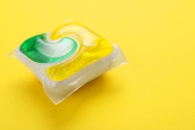 Photo of Dishwasher detergent pod on yellow background, closeup. Space for text