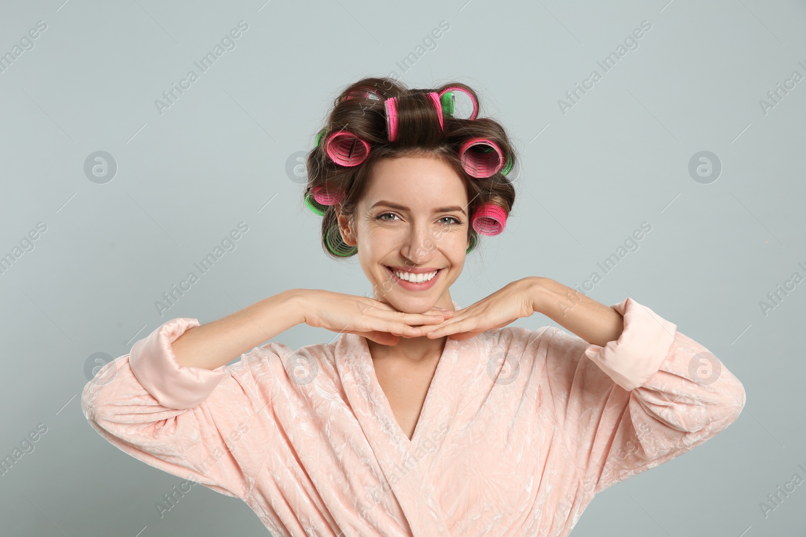 Photo of Beautiful young woman in bathrobe with hair curlers on light grey background