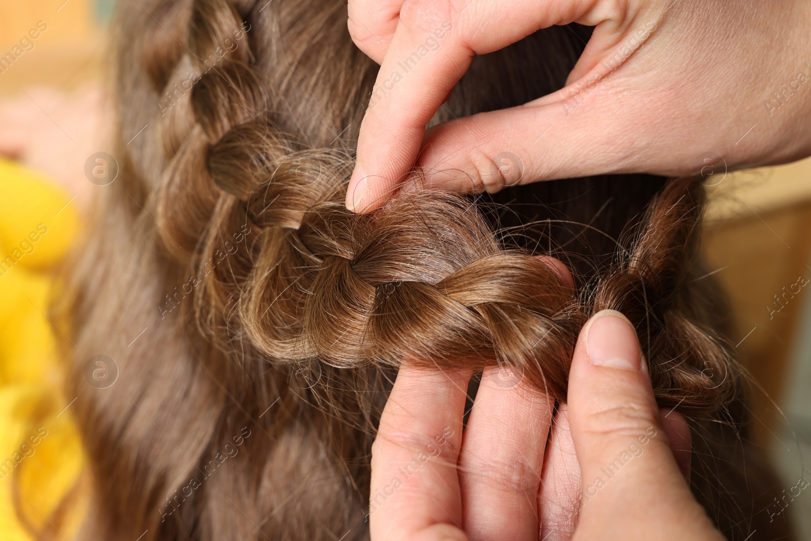 Photo of Professional stylist braiding girl's hair indoors, closeup