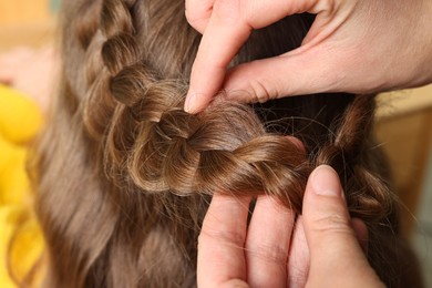 Photo of Professional stylist braiding girl's hair indoors, closeup