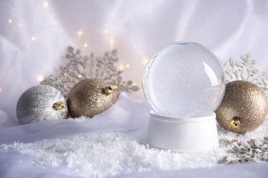 Photo of Magical empty snow globe with Christmas decorations on white fabric. Space for text