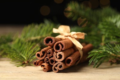 Photo of Bunch of cinnamon sticks and fir branches on wooden table, closeup