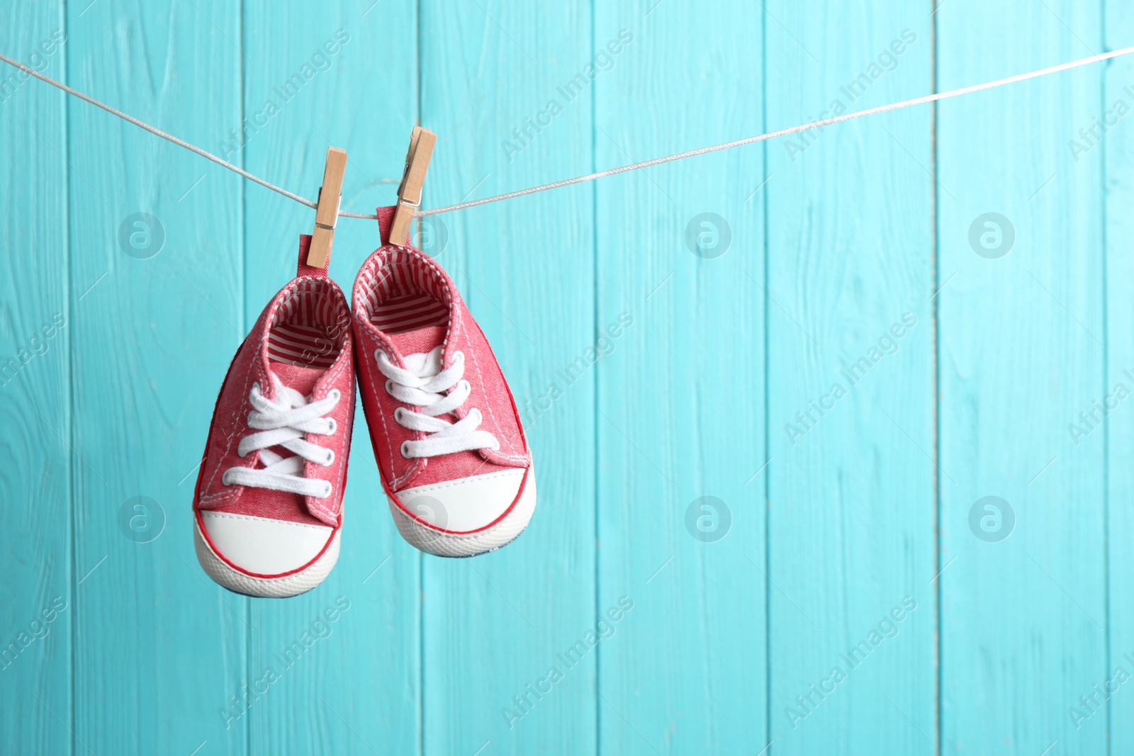 Photo of Baby shoes on laundry line against color wooden background, space for text. Child accessories