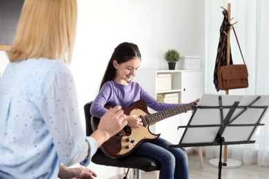 Photo of Little girl playing guitar with her teacher at music lesson. Learning notes