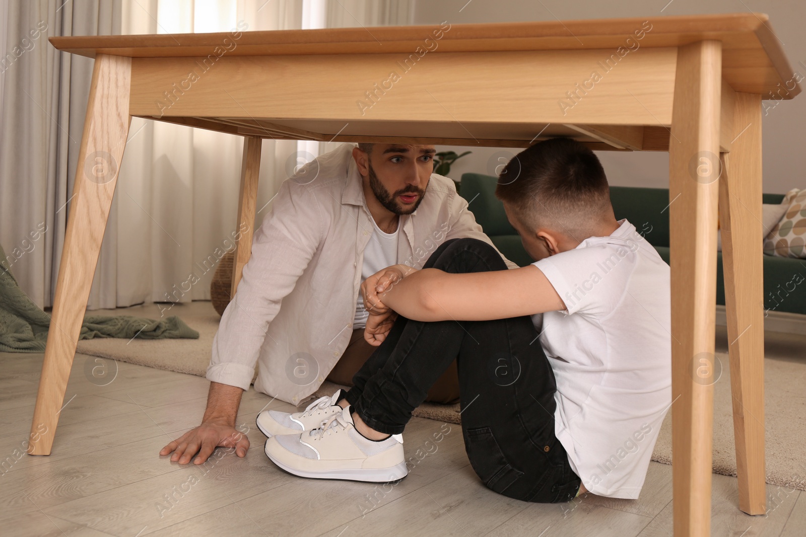 Photo of Father comforting his scared son under table in living room during earthquake