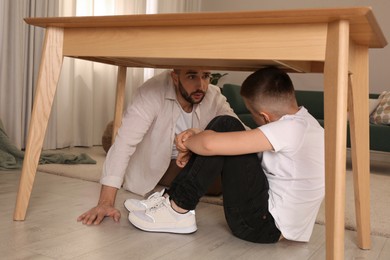 Photo of Father comforting his scared son under table in living room during earthquake