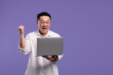 Emotional man with laptop on lilac background, space for text