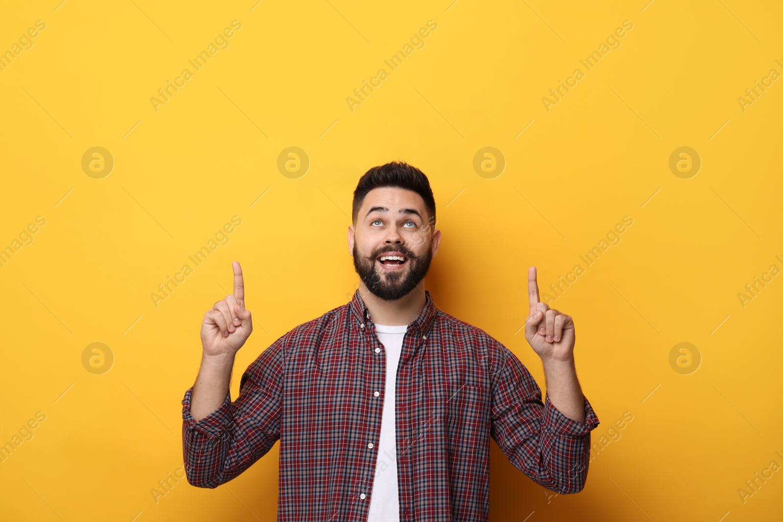 Photo of Happy young man with mustache pointing at something on yellow background. Space for text