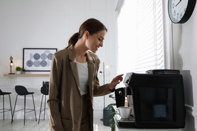 Young woman preparing fresh aromatic coffee with modern machine in office