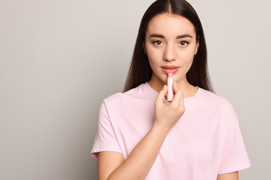 Photo of Young woman applying lip balm on grey background, space for text