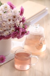 Photo of Fresh delicious herbal tea, books and beautiful bouquet on wooden table