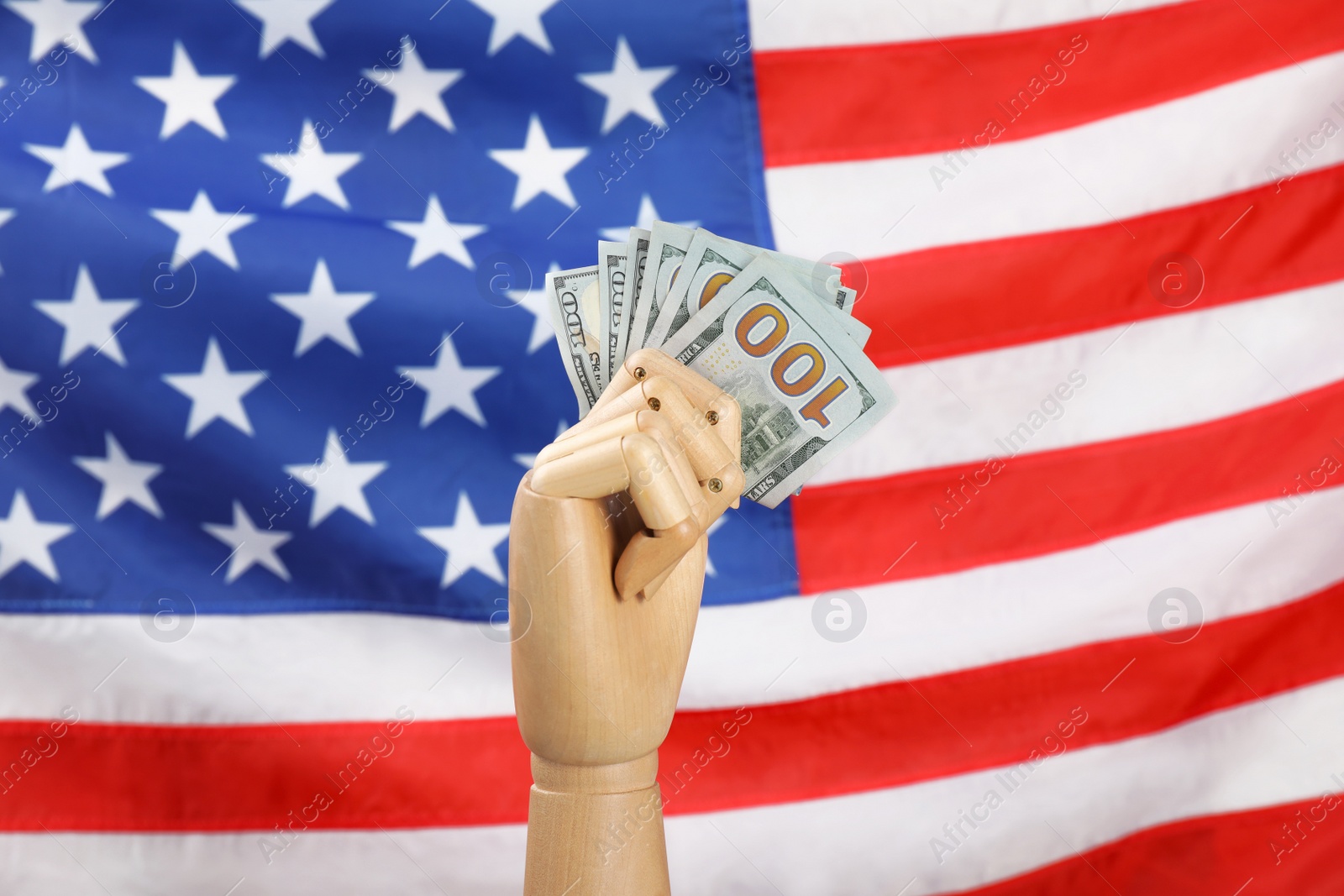 Photo of Wooden mannequin hand with fan of banknotes against USA national flag