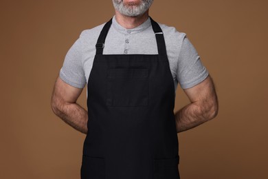 Photo of Man wearing kitchen apron on brown background, closeup. Mockup for design