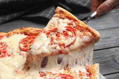 Photo of Woman taking slice of hot cheese pizza Margherita on table, closeup