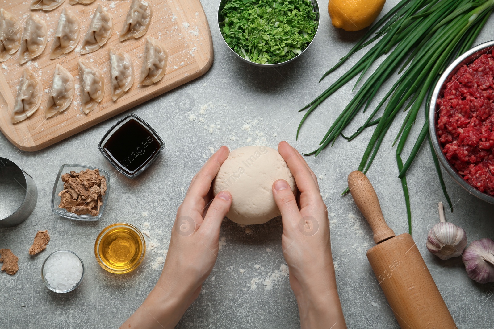 Photo of Woman cooking delicious gyoza at light grey table, top view