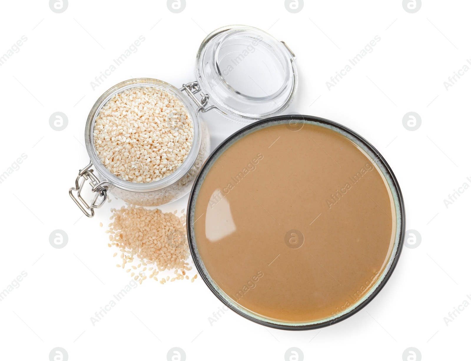 Photo of Bowl of tasty sesame paste, jar and seeds on white background, top view