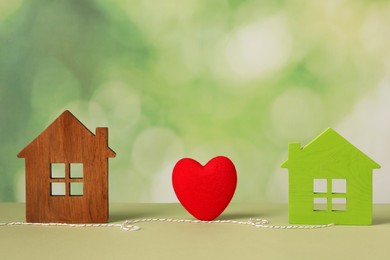 Photo of Red heart and decorative cord between two house models on light green background symbolizing connection in long-distance relationship
